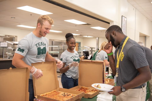 A man and woman serve a DeLand High School teacher lunch of pizza and wings
