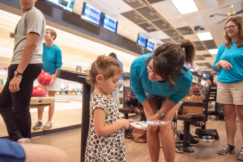 A woman gives a little girl a cookie at bowling alley 