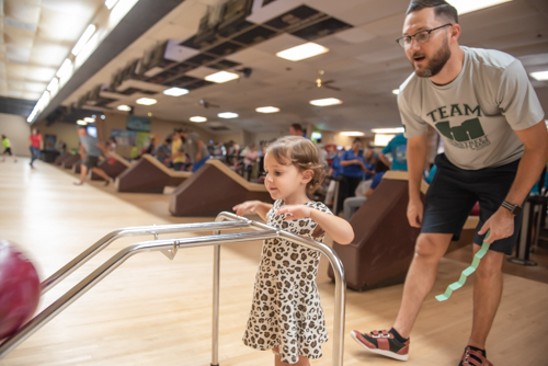A little girl bowls while her father encourages her at Bowling for Literacy Event in DeLand, FL