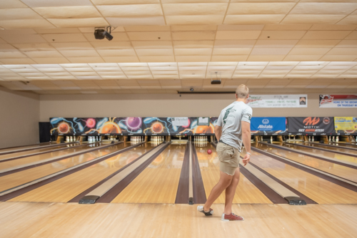 Man watches bowling ball roll towards pins at bowling alley in DeLand, FL