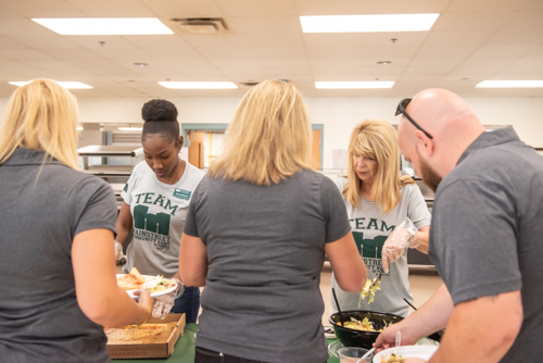 Two Mainstreet Community Bank employees serve teachers salad and pizza during lunch at DeLand High School