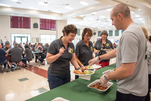 A man serves chicken wings to a teacher as other teachers eat lunch in the background at DeLand High School