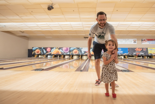 Little girl leads her father away from bowling lane after bowling with him