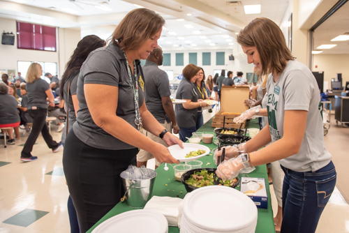 A Mainstreet Community Bank employee serves salad to a teacher while others eat lunch in the cafeteria of DeLand High School