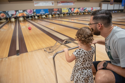 Little girl and father using bowling bar to play at bowling alley